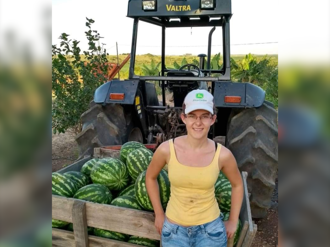 Agricultora Patrícia Vione parada atrás de um trator