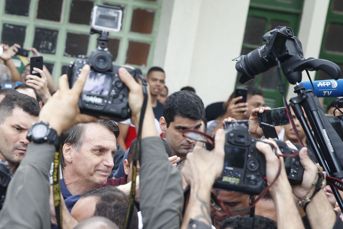 O candidato à Presidência Jair Bolsonaro (PSL) chega à seção eleitoral na Escola Municipal Rosa da Fonseca, na Vila Militar, acompanhado do filho Flávio Bolsonaro, que é candidato ao Senado. Agentes da Polícia Federal e militares do Exército fizeram a segurança do candidato. Tânia Rêgo/Agência Brasil