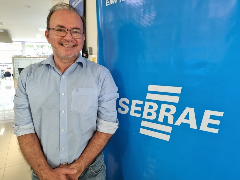 Homem em pé, ao lado de um banner, em que está escrito Sebrae 