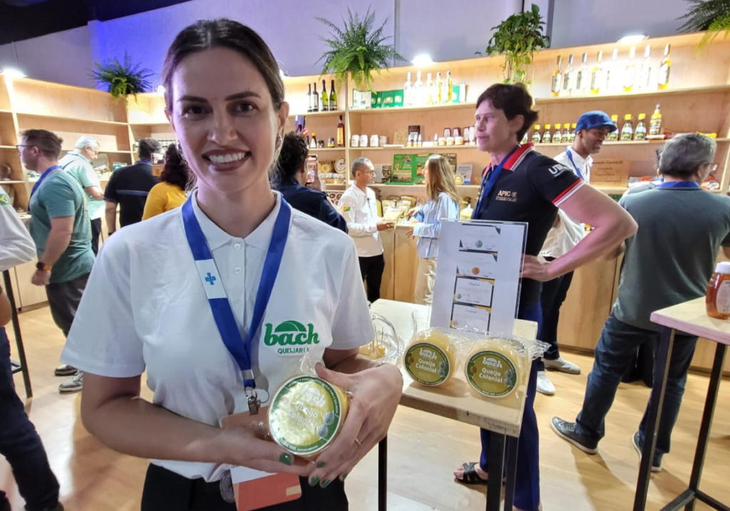 Uma mulher segurando em pé segurando e mostrando o queijo que produz