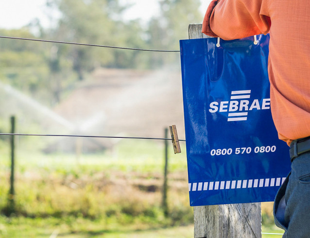 Homem segurando uma sacola do Sebrae e está olhando para o campo