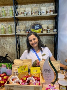Uma mulher que tem à sua frente uma bancada repleta de produtos que ela produz no Jalapão, Tocantins. A foto. é arquivo pessoal e foi tirada em uma feira que aconteceu em Macapá, Amapá