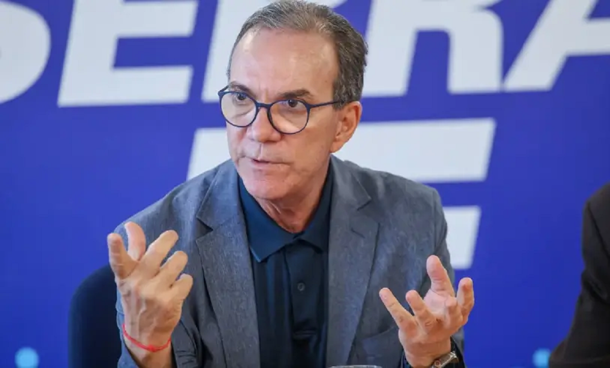 Foto do presidente do Sebrae. É um home que usa óculos e está sentado - gesticulando com as mãos. Ao fundo, há um painel escrito Sebrae.