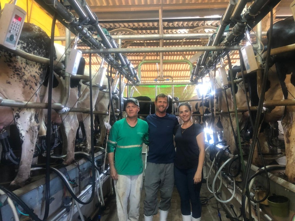 Na foto, aparecem três pessoas em meio a ordenha mecânica Na foto, aparecem três pessoas em meio a ordenha mecânica