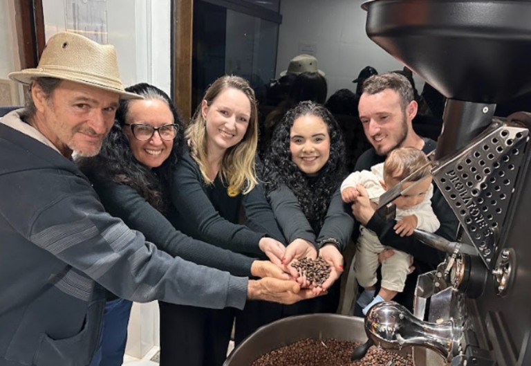 Na foto, há seis pessoas que apresentam grãos de cafés, entre elas, um bebê.