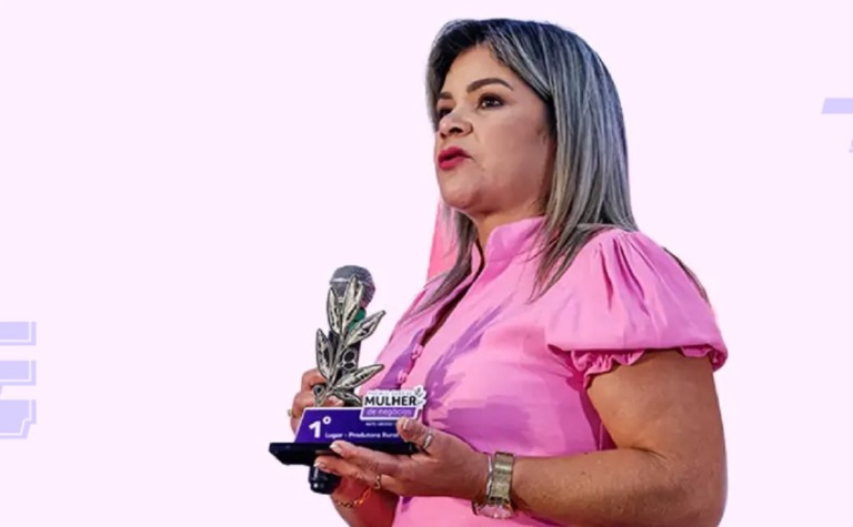 Mulher com uma blusa rosa, segurando um troféu