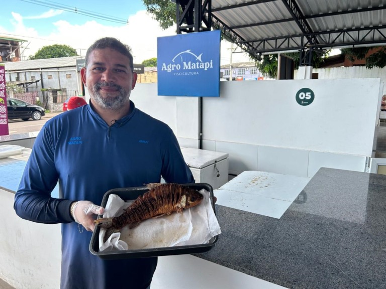 Com um peixe em uma assadeira e mostrando para câmera, um homem que veste uma camisa azul conta como empreendeu na piscicultura no Amapá
