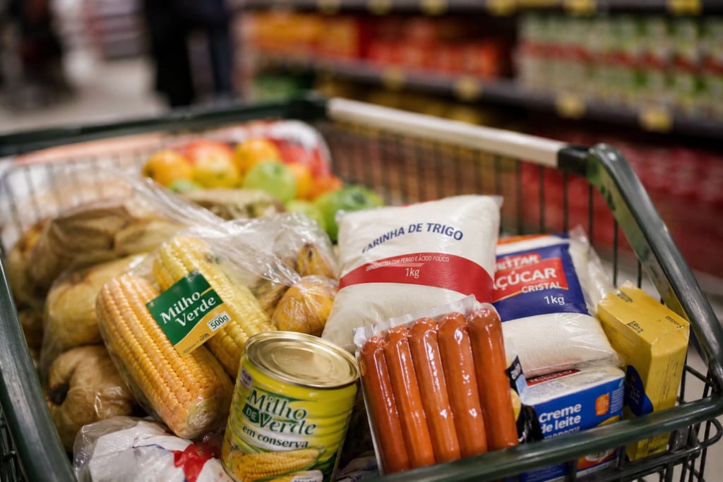 Imagem mostra carrinho de supermercado com comidas típicas de festa junina, como milho, salsicha e açúcar Imagem mostra carrinho de supermercado com comidas típicas de festa junina, como milho, salsicha e açúcar